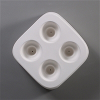 A square white ceramic mold for fusing hot glass on a grey background. Four separate identical circles have been carved into it with equal space between them. Each circle has a deeper circle carved in its center with a small vent hole in the center.