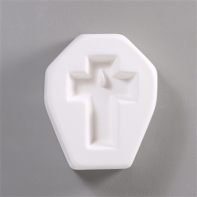 A white ceramic mold for fusing hot glass on a grey background. A simple cross shape has been carved into it. There is a post towards the top of the cross allowing for the resulting piece to be strung as jewelry.