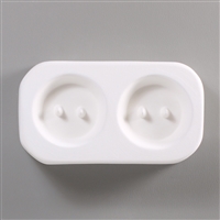 A rectangular white ceramic mold for fusing hot glass on a grey background. Two identical large circular buttons, each with two posts to create holes for threading, have been carved into it with equal space between them.