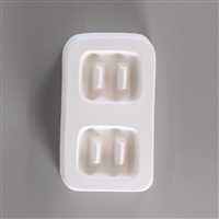 A rectangular white ceramic mold for fusing hot glass on a grey background. Two identical large square buttons, each with two long, thin posts to create holes for threading, have been carved into it with a space between them.