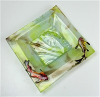 A square dish made from fused glass. The dish has a wide angled square rim and smaller flat base. The glass is marbled green, brown, and light green. The center has been textured with a koi fish, and two fused glass koi fish are also placed on the rim.