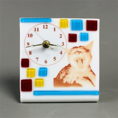 A rectangular piece of fused glass that has been bent to allow it to stand. It has a clock face printed on it as well as the image of a yawning cat. The clock has working hardware. The base glass is white, with additional red, yellow, and blue squares.