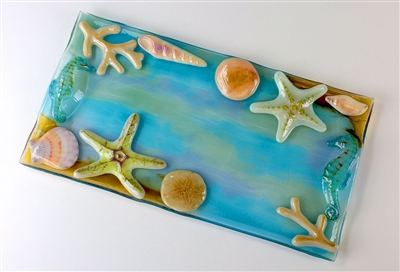 A rectangular tray of blue, green, and light purple streaked glass. The outside of the tray has been decorated with realistically colored glass shells and starfish. Two light blue seahorses cover the two semicircular handles on opposite sides.