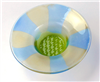 A round fused glass bowl with a wide rim and flat bottom. The wide rim is colored with alternating stripes of light blue and pale green radiating outwards, and the flat bottom is lime green and textured with a repeating geometric pattern.