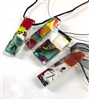 A variety of thick rectangular fused glass pendants hung from string and ribbon. Each pendant is made up of different colors and patterns of glass and are displayed on a white background.