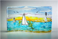 A rectangle of glass shaped into an S-curve standing on its side. The glass shows a design of two white sailboats on bright blue waves. There is a tan island with a white lighthouse to the right, and the sky is a sunset gradient from orange to blue.