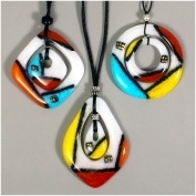 Three fused glass pendants hang from black cords. Each pendant has an outer ring with a smaller shape inside it. The top left are squares, top right circles, and the bottom teardrops. They are white with black lines sectioning off bright colored accents.