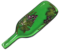 A green glass bottle that has been shaped into a dish with the neck remaining raised as the handle. The body of the bottle has been decorated with purple glass grapes, green glass grape leaves, and brown glass stems.