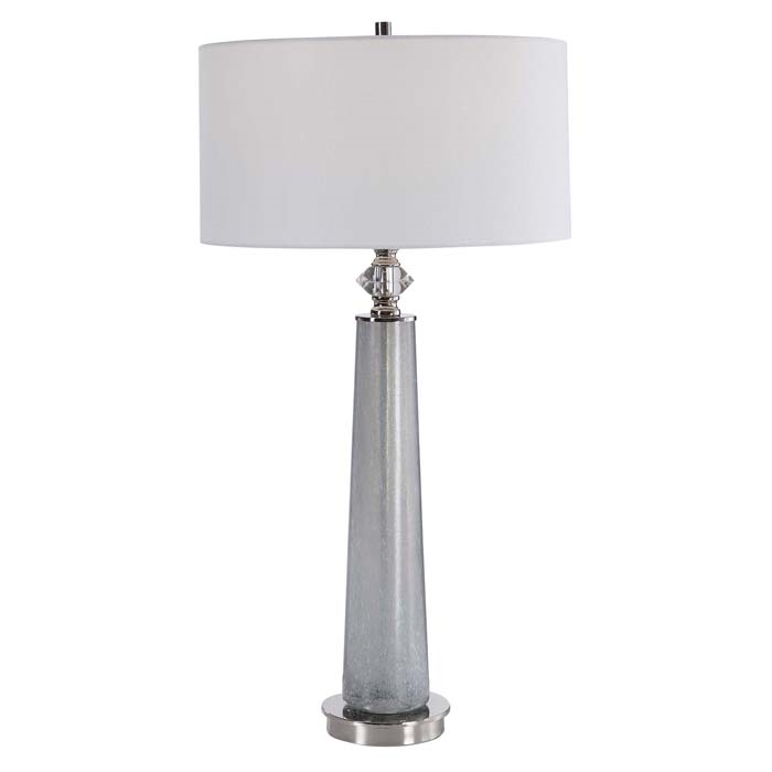 Grayton Modern Lamp. This sleek table lamp features a frosted art glass base in light gray with white speckled texture. The piece is accented by polished nickel details and a crystal ornament. The hardback drum shade is covered in a white linen fabric.