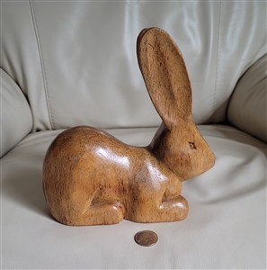 A hand carved wooden bunny rabbit sculpture with a natural light wood finish shown from the side to highlight the grain and primitive carving style
