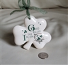 Preowned 1994 Russ Berrie porcelain shamrock hanging ornament with green ribbon that reads God Bless the Irish next to a quarter for size scale