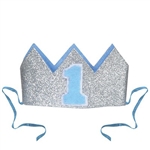 The Glittered Baby's 1st Birthday Crown is a silver glittered crown with light blue lining and a blue "1" on the front. It has two detachable ribbon ties and measures 4 1/2 inches wide and 2 1/2 inches tall. Contains one (1) per pack. No returns.